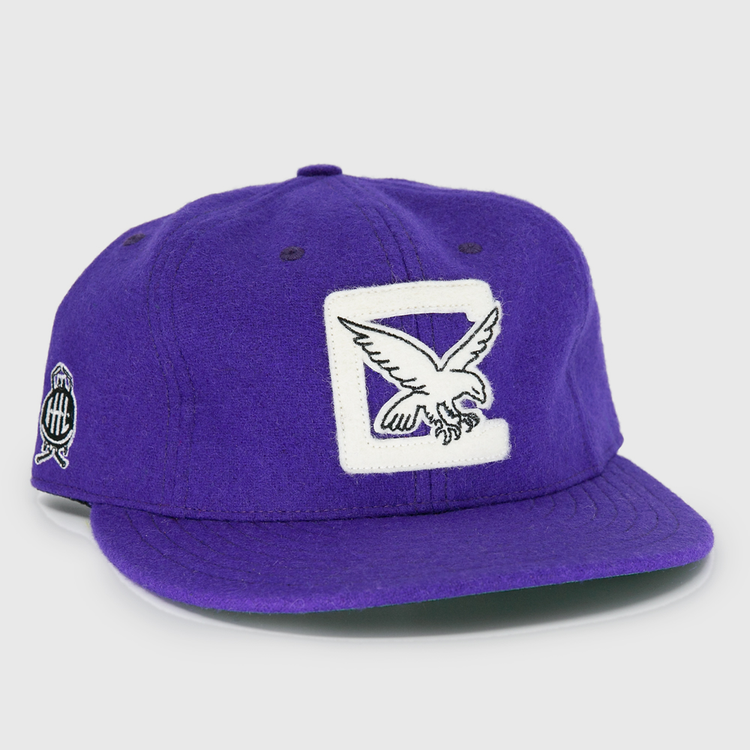 The EFF Cleveland Falcons 1936 Vintage Ballcap is a purple wool cap with a white patch and embroidered flying eagle on the front, a circular black and white logo on the side, and an adjustable leather strap for a custom fit.