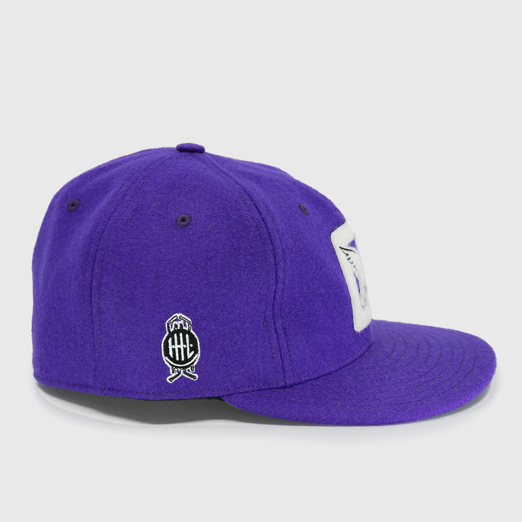 The EFF Cleveland Falcons 1936 Vintage Ballcap is a purple wool cap with a white rectangular front patch, a black and white circular side logo featuring crossed bats, and an adjustable leather strap for the perfect fit.