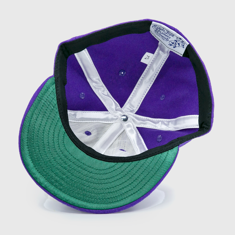 The EFF Cleveland Falcons 1936 Vintage Ballcap is a purple wool cap shown upside down, displaying its green underbrim, white inner lining, sewn crown labels, and an adjustable leather strap.