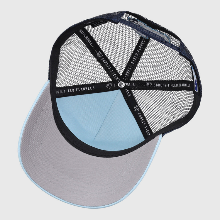 A top-down view of the Columbus Clippers MiLB Trucker Ballcap by Ebbets Field shows a light blue crown, gray brim, black mesh back, and 