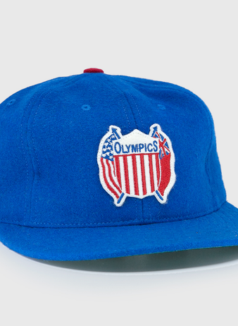 The EFF Detroit Olympics Vintage Ballcap is a blue wool cap with a red, white, and blue USA-shaped Olympic patch, a smaller white and black side patch, and an adjustable leather strap for a great fit.