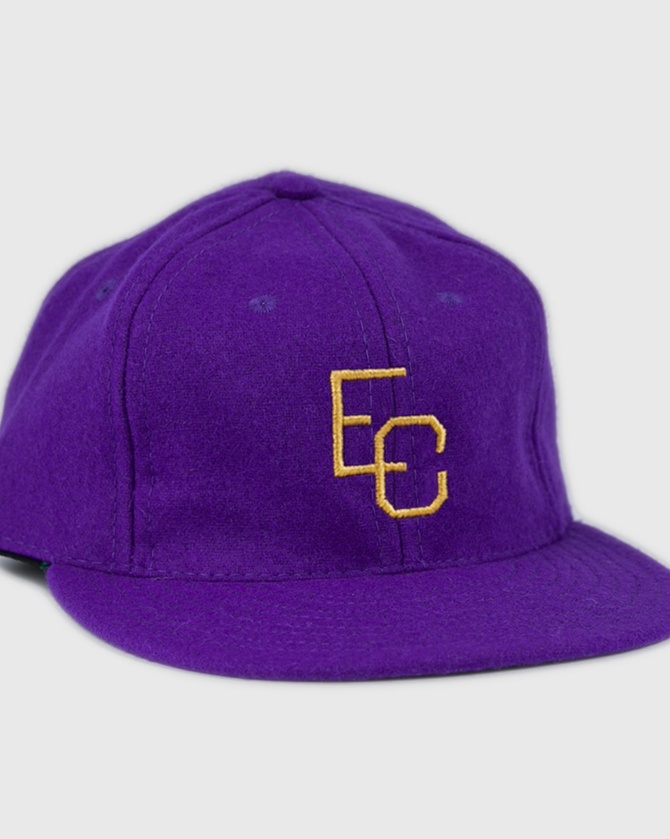 The Ebbets Field Flannels East Carolina University 1961 Vintage Ballcap is a purple wool cap with interlocking yellow EC letters on the front, shown at a slight angle against a white background.