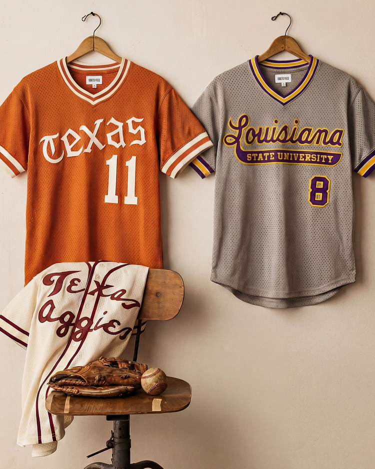Two sports jerseys hang on a wall: an orange Texas 11 jersey and an Ebbets Field Louisianna State University 1987 V-Neck Mesh Jersey. Below, a Texas Aggies towel, baseball glove, and ball sit on a wooden stool.