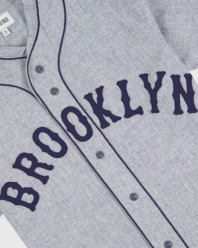 The Brooklyn Eagles 1935 Authentic Wool Road Jersey by Ebbets Field features a gray wool construction with dark blue piping and buttons, highlighted by large dark blue “BROOKLYN” lettering across the chest—a faithful Negro Leagues reproduction inspired by the iconic original Brooklyn Eagles jersey.