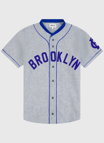 The Ebbets Field Brooklyn Royal Giants 1915 Authentic Wool Road Jersey features a gray short-sleeve design with blue piping and BROOKLYN in bold blue letters across the chest, inspired by the classic 1915 team jersey. It has a blue logo on the left sleeve and front button closure.