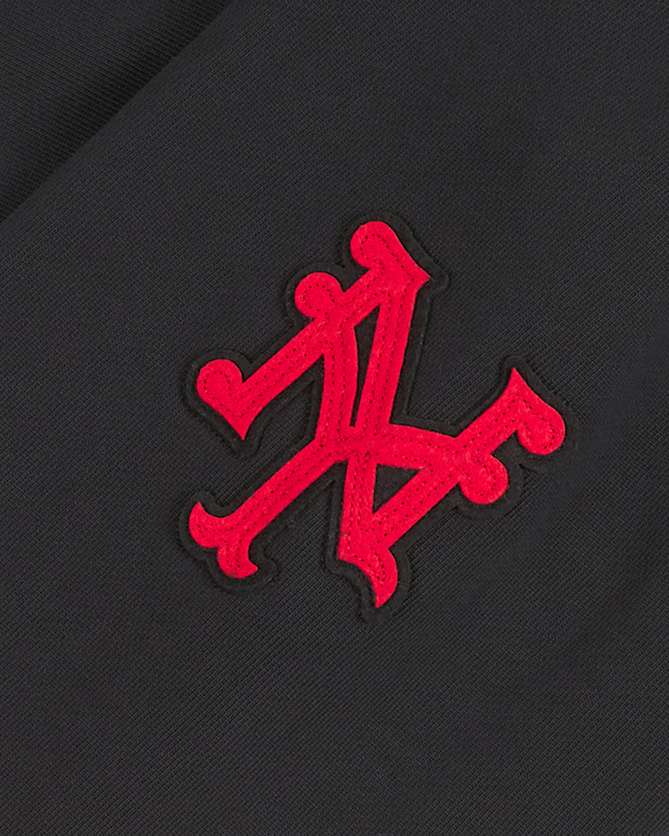 A red, ornate KL monogram is embroidered on a black fabric background, adding a distinct touch of style to the New York Cubans Heavyweight Cotton Terry Pullover Hoodie by Ebbets Field—an elevated piece inspired by classic Negro League apparel.
