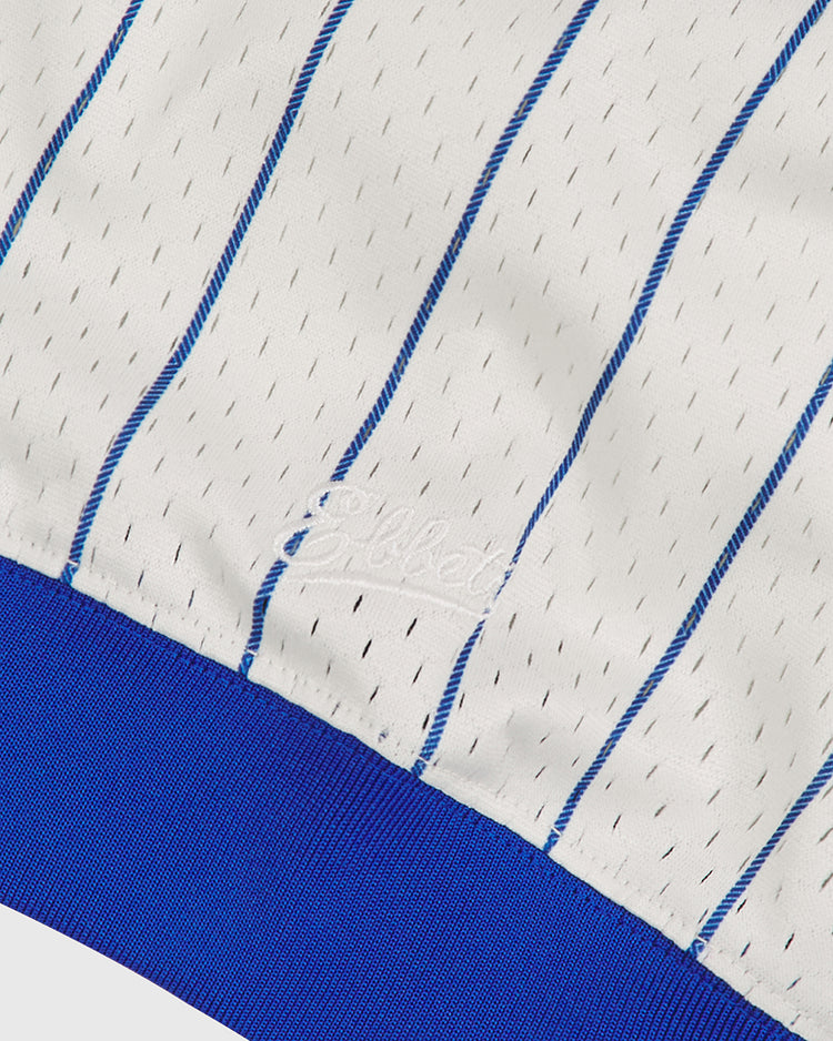 Close-up of white mesh fabric featuring thin blue pinstripes, fine black stitching, and a bold blue band along the hem. Inspired by vintage baseball jerseys, “Elite” is delicately embroidered in white thread—a classic touch often found in premium Negro Leagues apparel. This detail enriches the Brooklyn Royal Giants 1925 V-Neck Mesh Jersey by Ebbets Field.