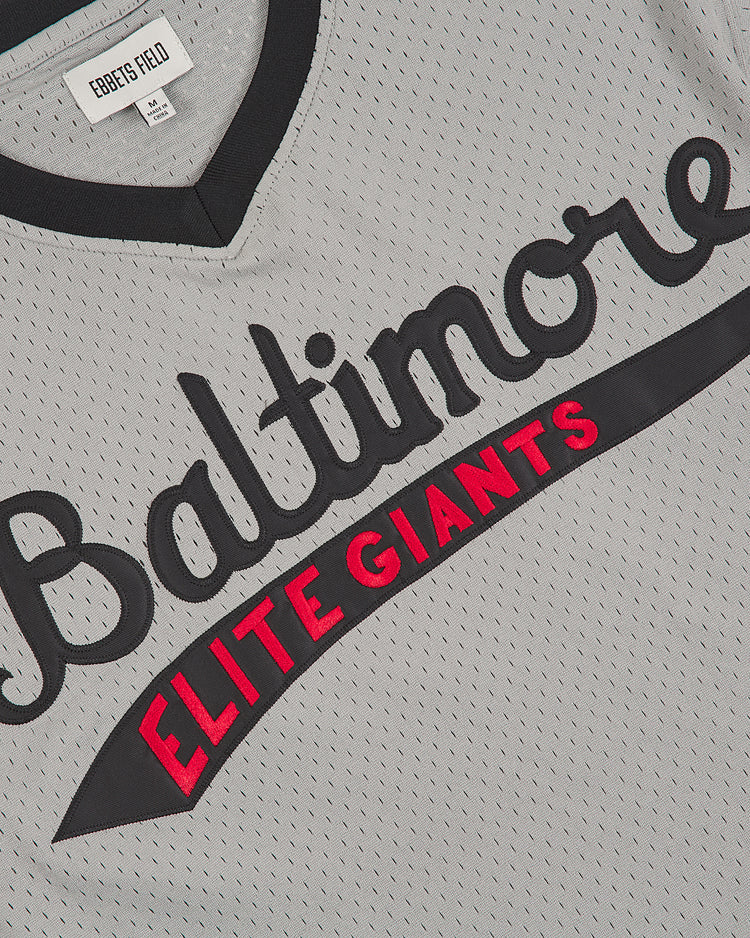 A detailed shot of the Baltimore Elite Giants 1949 V-Neck Mesh Road Jersey by Ebbets Field, showcasing its classic gray mesh fabric with “Baltimore” in black script and “ELITE GIANTS” in bold red lettering. This authentic Negro League road jersey features a V-neck design, with an Ebbets Field collar label.