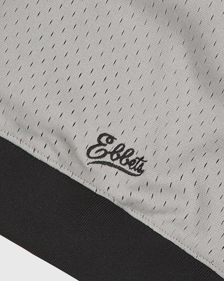 Close-up of a light gray mesh fabric with small perforations, featuring “Ebbets Field” embroidered in black script above a thick black band at the bottom—a design inspired by the authentic Baltimore Elite Giants 1949 V-Neck Mesh Road Jersey.