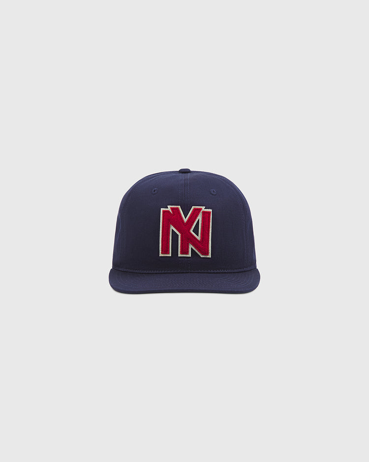The Brooklyn Eagles Cotton Twill Ballcap by Ebbets Field is a navy blue baseball cap with a striking red and white embroidered “N” and “K” logo on the front, shown against a plain light gray background.