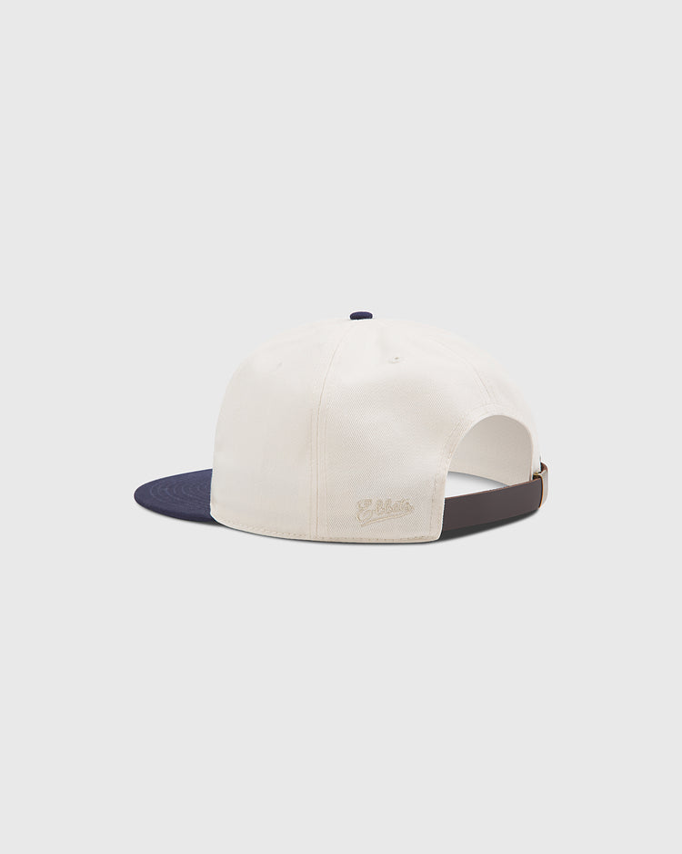 The New York Cubans Authentic Cotton Ballcap by Ebbets Field is shown from the back, featuring cream-colored cotton twill with a navy blue brim. It has an adjustable brown strap and a small embroidered logo on the side, echoing classic Negro League hat style. The background is plain light gray.