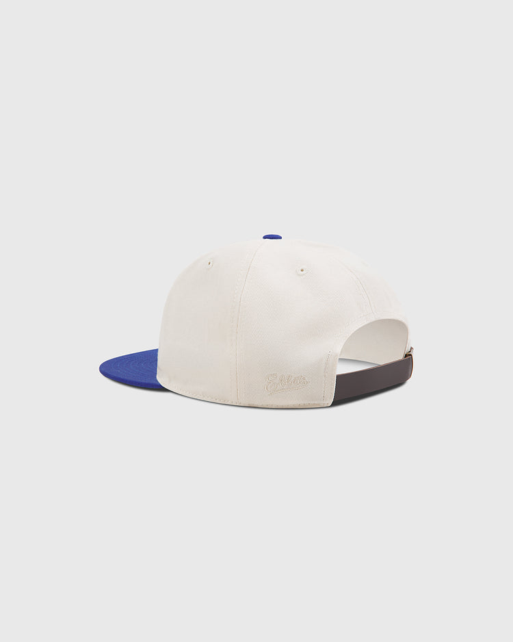 The Ebbets Field Brooklyn Royal Giants Cotton Twill Ballcap is pictured from the back, showcasing its cream-colored cotton twill fabric, blue brim, and adjustable brown strap with a metallic buckle—all set against a plain white background as a tribute to Black baseball history and the enduring legacy of the Brooklyn Royal Giants.
