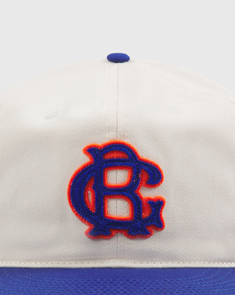 A close-up of the Ebbets Field Brooklyn Royal Giants Cotton Twill Ballcap, featuring a white and blue design with a blue “B” logo outlined in red on the front, inspired by the Brooklyn Royal Giants and celebrating Black baseball history.