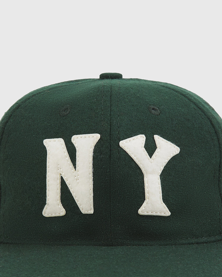 The Ebbets Field NY Black Yankees Authentic Wool Ballcap, shown from the front against a plain light background, features dark green wool fabric and prominent white “NY” lettering—evoking the classic style of the New York Black Yankees from the Negro National League. Only the top portion of the cap is visible in the image.