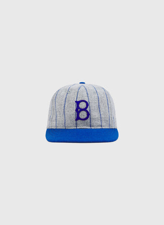 The Brooklyn Royal Giants Authentic Wool Ballcap by Ebbets Field features a gray wool design with blue vertical stripes, a blue brim, and a prominent blue “B” embroidered on the front, paying tribute to the legendary Brooklyn Royal Giants and celebrating Black baseball history. The classic cap is shown against a plain white background.