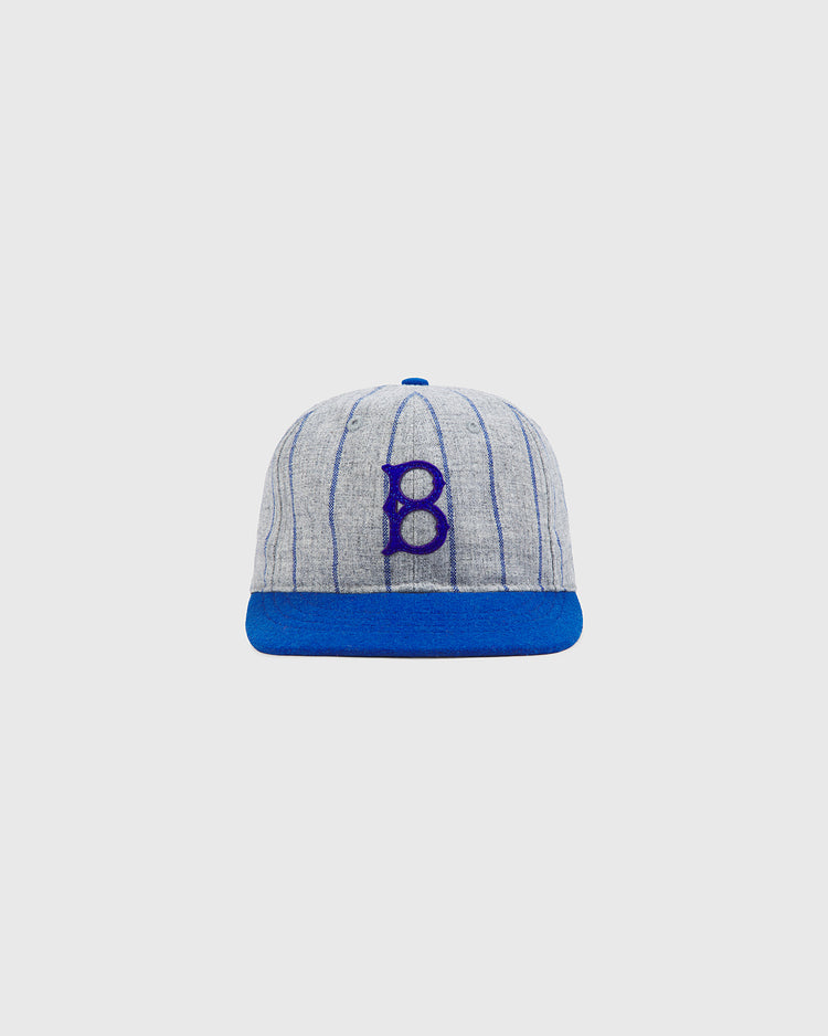 The Brooklyn Royal Giants Authentic Wool Ballcap by Ebbets Field features a gray wool design with blue vertical stripes, a blue brim, and a prominent blue “B” embroidered on the front, paying tribute to the legendary Brooklyn Royal Giants and celebrating Black baseball history. The classic cap is shown against a plain white background.