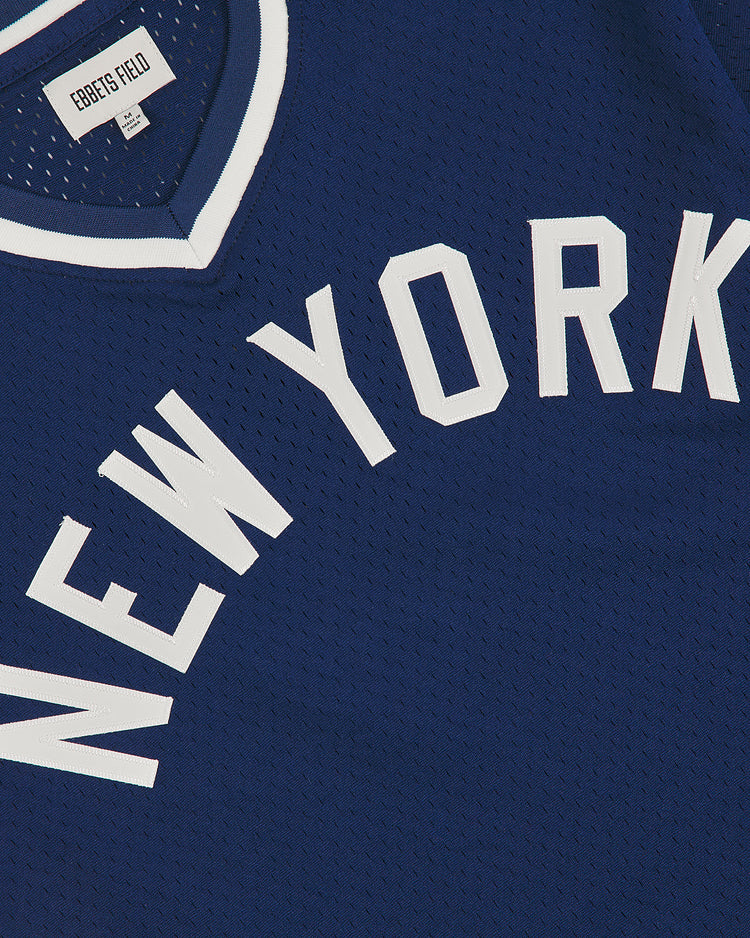 The NY Black Yankees V-Neck Mesh Jersey by Ebbets Field features a blue mesh construction with white trim around the collar and “NEW YORK” displayed in bold, white uppercase letters across the front. Inspired by classic Negro National League designs, a tag inside the collar is marked with “Ebbets Field.”.