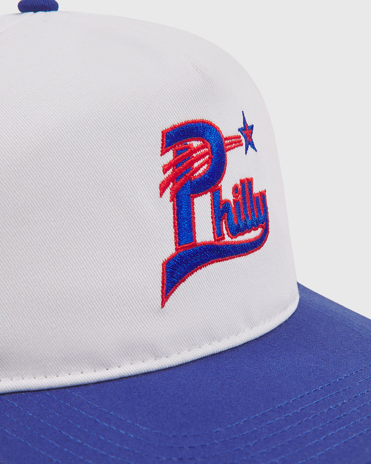 The Ebbets Field Philadelphia Stars A-Frame Cotton Twill Ballcap is a white hat with a blue brim, showcasing a stylized red, white, and blue Philly logo with a star on the front—drawing inspiration from classic Philadelphia Stars snapback and retro baseball hat designs.
