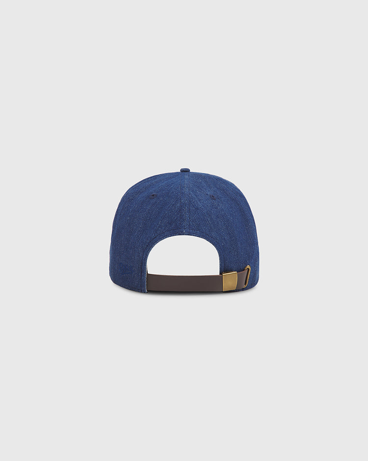 The Ebbets Field Kansas City Katz Indigo Cotton Denim Ballcap is shown from the back, highlighting its adjustable brown strap with a gold-colored buckle. Inspired by classic Kansas City Katz style, this blue denim cap stands out against a plain, light gray background.