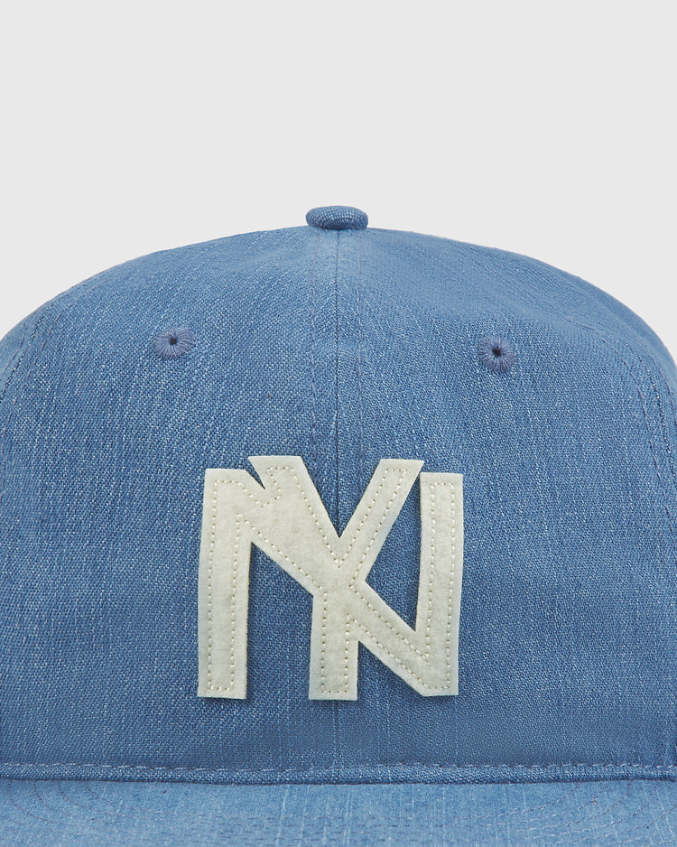The Ebbets Field New York Brooklyn Eagles Indigo Cotton Denim Ballcap features a white, stylized NY logo stitched on the front—subtly honoring classic teams like the Brooklyn Eagles of the Negro Leagues. The background is plain and light-colored.