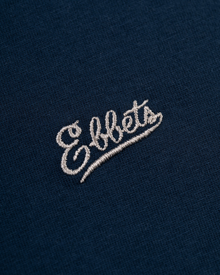 Close-up of the Ebbets Chest Logo Long Sleeve Pocket Tee by Ebbets Field Flannels, featuring durable navy cotton and Ebbets embroidered in white cursive—a timeless wardrobe staple.