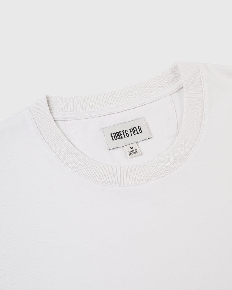 Close-up of the collar and upper chest of the Ebbets Chest Logo Short Sleeve Tee by Ebbets Field Flannels, made from durable cotton with a visible brand label and size M tag, laid flat on a white background.