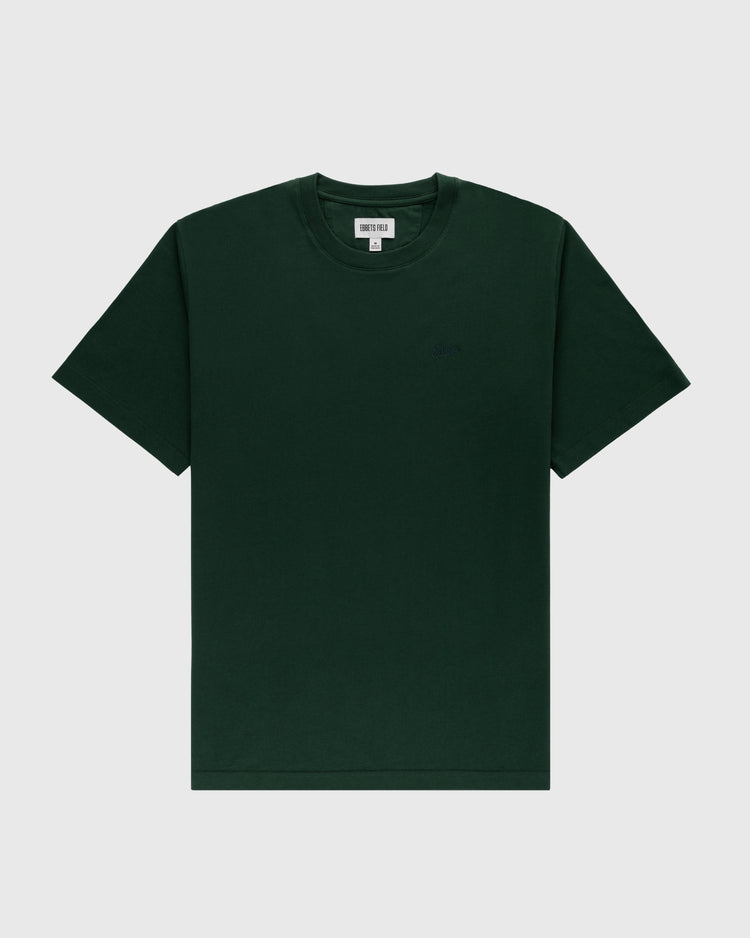 The Ebbets Chest Logo Short Sleeve Tee by Ebbets Field Flannels is a dark green cotton crew neck t-shirt with short sleeves, shown on a light gray background and featuring a small inner neckline tag.