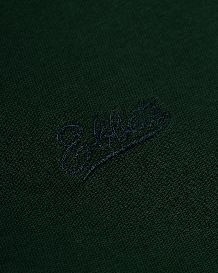 Close-up of dark green Ebbets Chest Logo Short Sleeve Tee by Ebbets Field Flannels, featuring a durable cotton build and an embroidered cursive script Ebbets logo in dark thread—an essential wardrobe staple.