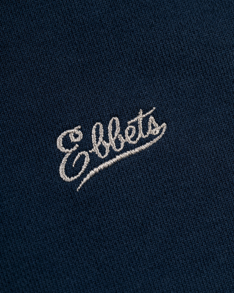 Close-up of the blue Ebbets Field Flannels Chest Logo Heavyweight Cotton Terry Pullover Hoodie, featuring Ebbets embroidered in white cursive.
