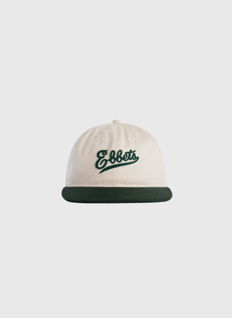 The Ebbets Felt Script Cotton Twill Ballcap by Ebbets Field Flannels features cream cotton twill, a dark green brim, and Ebbets embroidered in green script on the front, shown against a plain light gray background.