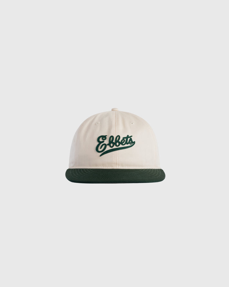 The Ebbets Felt Script Cotton Twill Ballcap by Ebbets Field Flannels features cream cotton twill, a dark green brim, and Ebbets embroidered in green script on the front, shown against a plain light gray background.