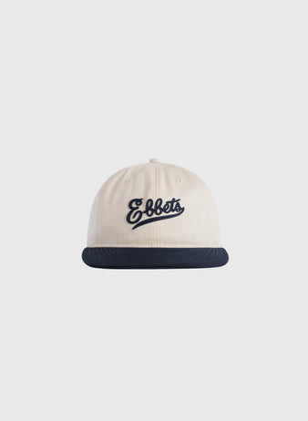 The Ebbets Felt Script Cotton Twill Ballcap by Ebbets Field Flannels is cream-colored with a dark blue brim and features Ebbets embroidered in dark blue script on the front.