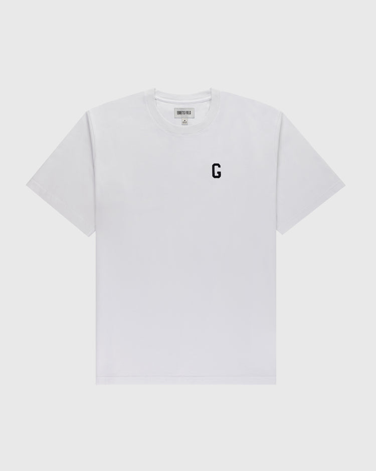 The Ebbets Field Flannels Homestead Grays Embroidered G Short Sleeve Tee is a white shirt featuring a small black ‘G’ honoring Josh Gibson on the left chest, shown against a light gray background.