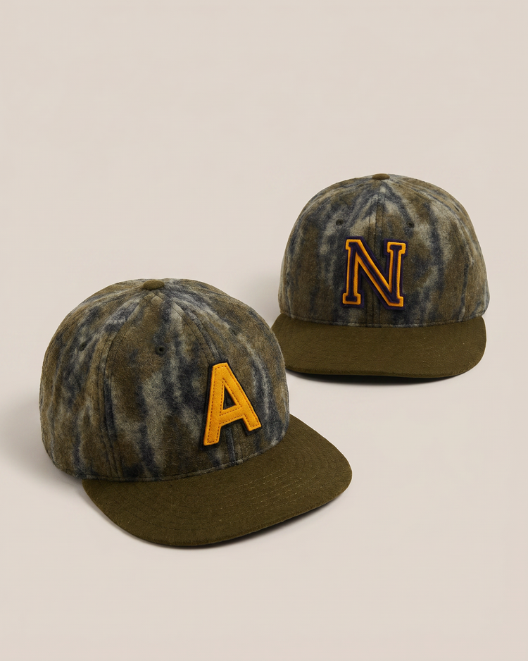 The Ebbets Field Mossy Oak x Ebbets Field 1947 Navy Ballcap collection features two tie-dye baseball caps with olive brims, inspired by Navy Academy designs—one with a yellow 
