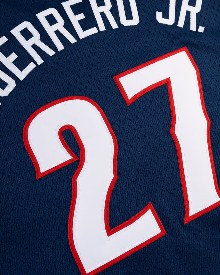 A close-up of the Ebbets Field VLAD GUERRERO JR BUTTON UP MESH JERSEY in navy, featuring white and red trim, with Guerrero Jr.’s name and the number 27.