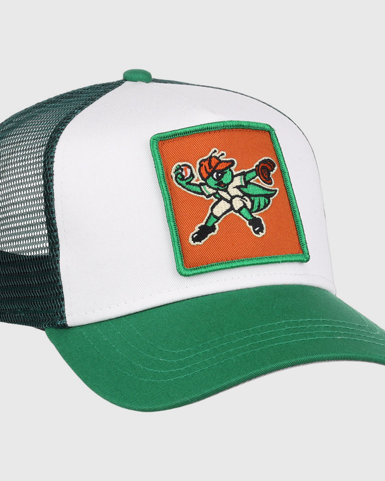 The Greensboro Grasshoppers MiLB Trucker Ballcap by Ebbets Field is a green and white mesh-back hat featuring a front patch with a cartoon leprechaun mascot in a fighting stance on an orange background.