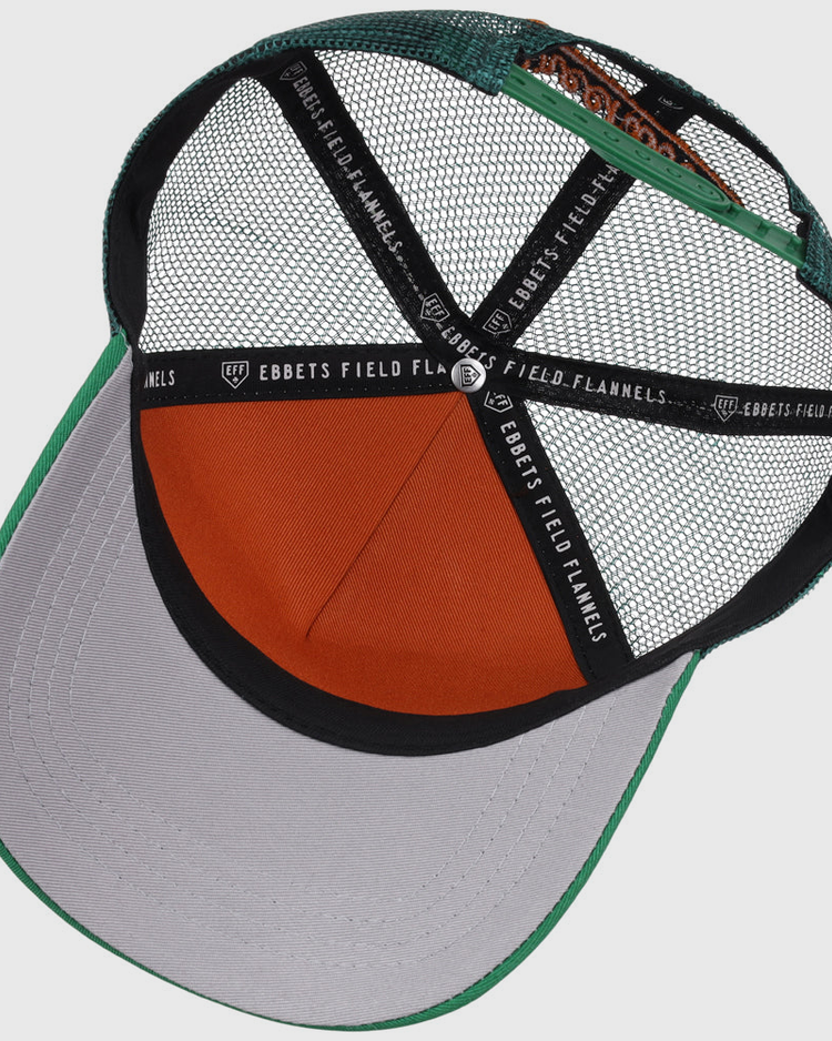 The inside view of the Greensboro Grasshoppers MiLB Trucker Ballcap by Ebbets Field shows green, gray, and orange mesh panels, an orange sweatband, and black straps labeled “EBBETS FIELD FLANNELS.”.