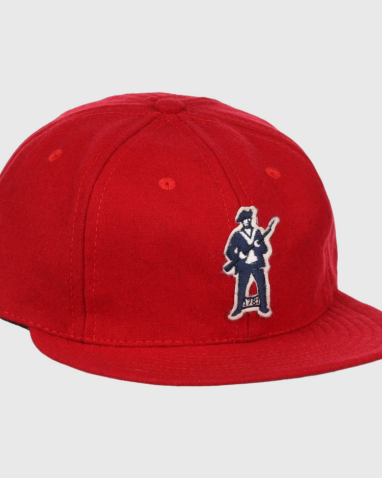 The EFF Greensboro Patriots 1922 Vintage Ballcap is a bright red hat with an embroidered figure in a suit holding a guitar on the front left side.
