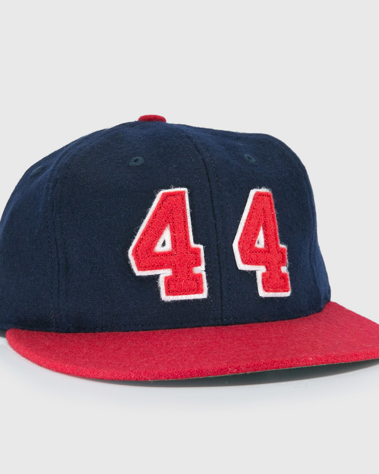 The Ebbets Field Flannels Hank Aaron 1957 Signature Series Ballcap is a vintage-style wool cap in navy with a red brim and bold red-and-white “44” on the front, inspired by baseball legends and proudly made in the USA.