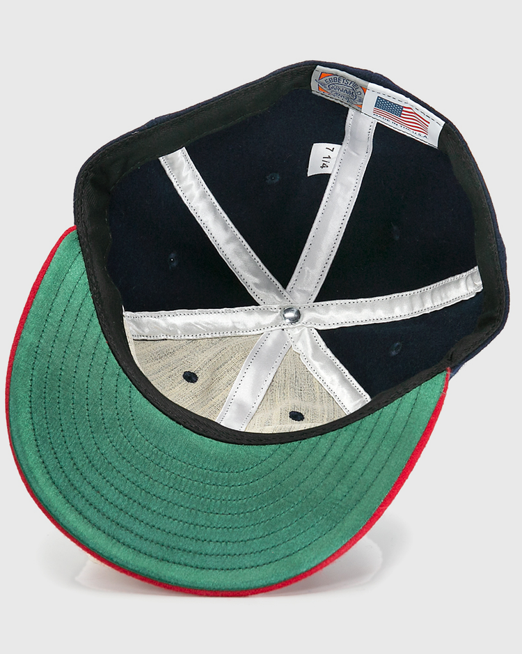 An inside view of the Ebbets Field Flannels Hank Aaron 1957 Signature Series Ballcap shows a green underbrim, red trim, white stitched panels, silver top button, and an American flag tag, highlighting its USA-made quality.