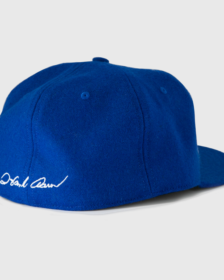 The Hank Aaron 1973 Signature Series Ballcap by Ebbets Field Flannels is a royal blue vintage wool cap, made in the USA, shown from the back left with a white embroidered signature above the brim.