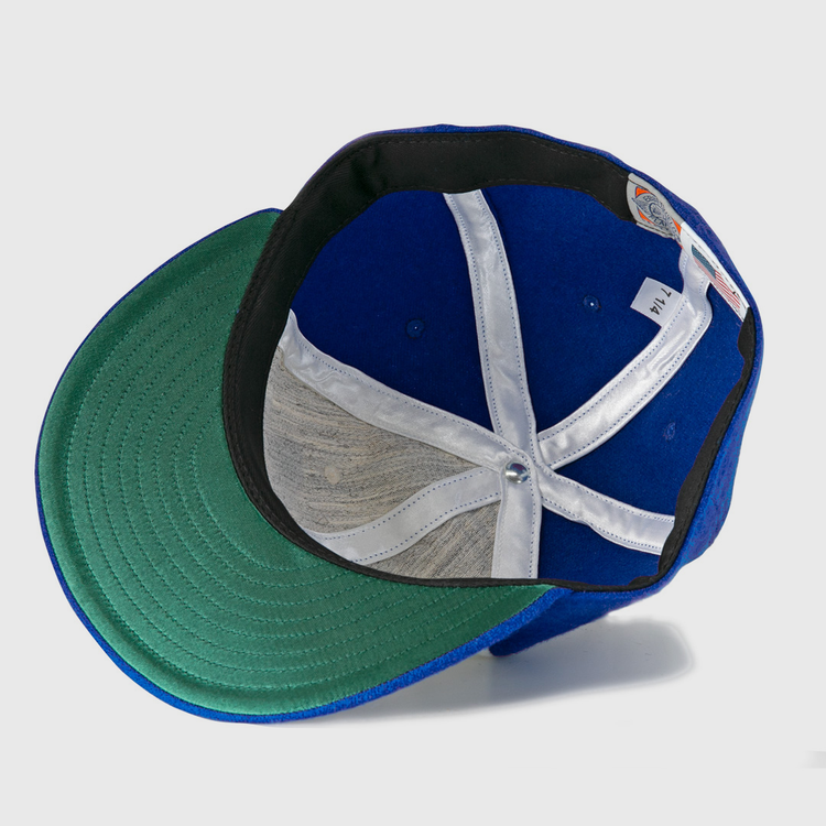 The Hank Aaron 1973 Signature Series Ballcap by Ebbets Field Flannels is a blue vintage wool cap shown from below, highlighting its green under-brim, white hatband, and inner structure with a central metal button.