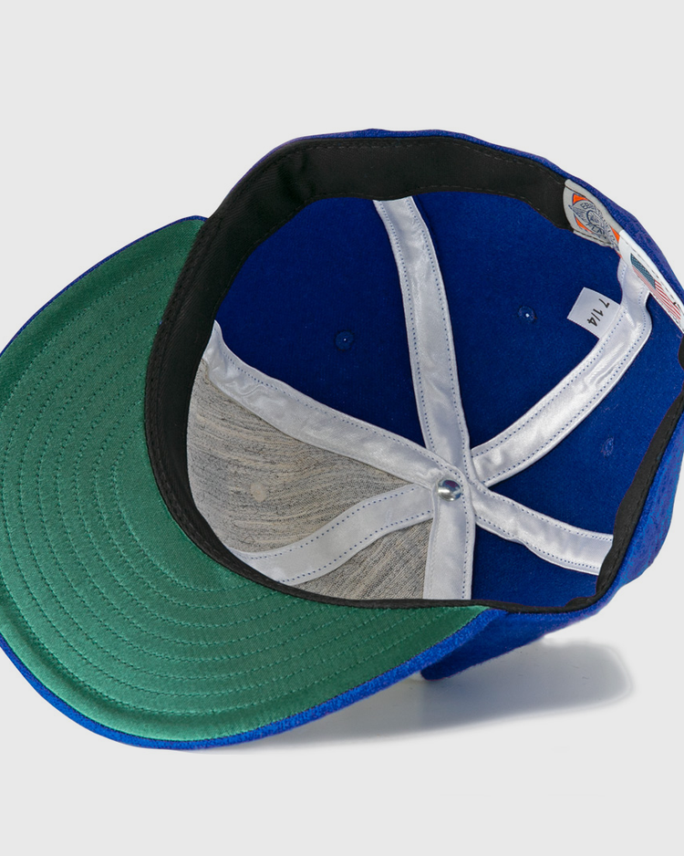 The Hank Aaron 1973 Signature Series Ballcap by Ebbets Field Flannels is a blue vintage wool cap shown from below, highlighting its green under-brim, white hatband, and inner structure with a central metal button.