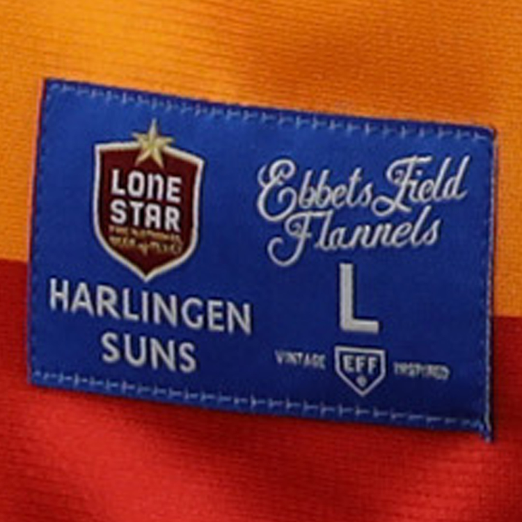 A blue label on orange and red fabric reads “EFF” and “Harlingen Suns,” featuring the Harlingen Suns EFF Lone Star Baseball Jersey by EFF, with vintage details honoring Texas baseball and the Lone Star League.