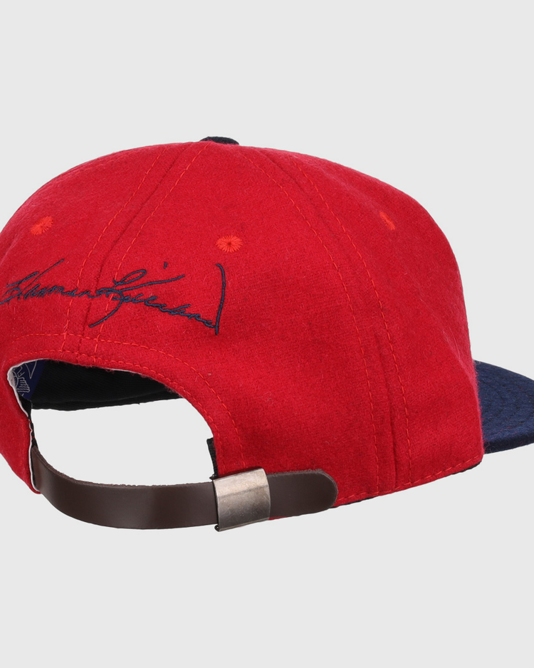 The Ebbets Field Flannels Harmon Killebrew Signature Series Ballcap, in red and navy vintage wool, is shown from the back with a brown adjustable strap, metal clasp, and black signature embroidery above the opening.