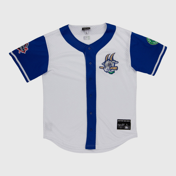 The Ebbets Field Hartford Yard Goats MiLB Button Down Jersey is white with blue sleeves and trim, a cartoon goat logo on the chest, sleeve patches, button-down front, and a black label near the hem.