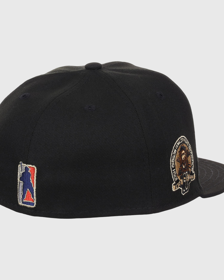 The EFF Homestead Grays Josh Gibson Fitted Ballcap in black is shown from an angled rear view, featuring a multicolor embroidered back logo and a lion patch with text on the left side, inspired by classic Negro Leagues cap designs.