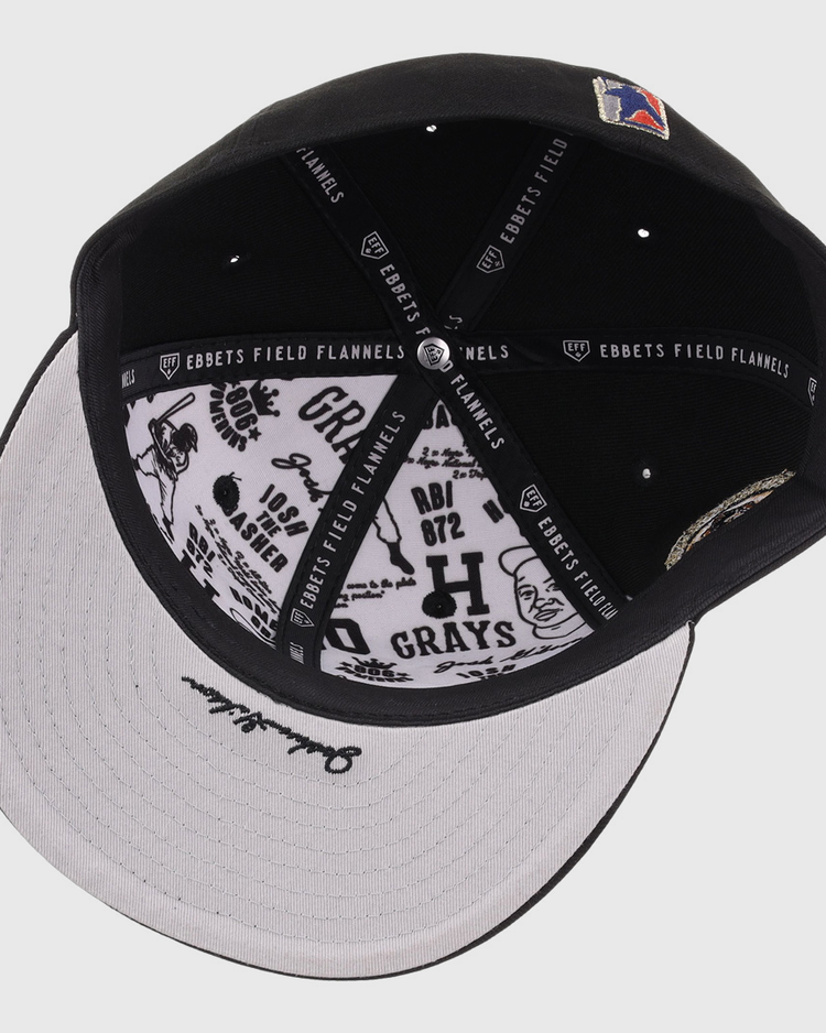 The Homestead Grays Josh Gibson Fitted Ballcap - Black by EFF is shown from above, highlighting its inner lining with EFF branding and black graphic designs and text on the white underside of the brim.