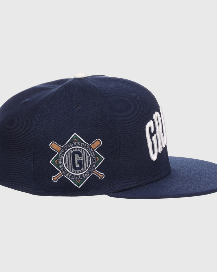 The EFF Homestead Grays NLB Flip Fitted Ballcap features a navy flat-brim, bold white GRD letters up front, and a diamond patch with bats and G logo on the side, honoring Pittsburgh’s legendary Homestead Grays.