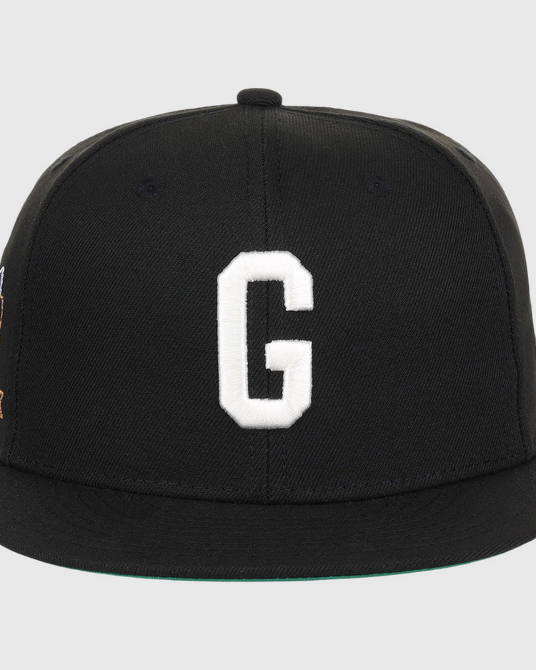 The Ebbets Field Homestead Grays NLB Tc Fitted Ballcap is a black cap with a flat brim, featuring a large white embroidered letter G on the front and minimal visible detailing.